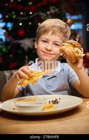 Happy Boy si diverte a gustare deliziosi panini nel ristorante durante le festività invernali Foto Stock