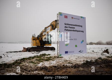 Fehmarn, Germania. 7 dicembre 2023. Un cartello con la scritta "Rail link to the Fehmarnbelt Fixed Link" è allegato a un escavatore, che può essere visto in un campo durante una cerimonia della Deutsche Bahn. Con la cerimonia, la Deutsche Bahn ha dato il segnale a Fehmarn per la costruzione del collegamento ferroviario con il previsto tunnel del Mar Baltico. Il percorso ferroviario lungo 88 chilometri tra Puttgarden e Lübeck collegherà la strada e il tunnel ferroviario previsti alla rete ferroviaria tedesca a partire dal 2029. Credito: Christian Charisius/dpa/Alamy Live News Foto Stock