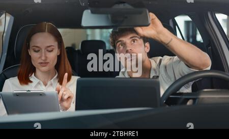 Uomo caucasico acquirente cliente che sceglie prova nuovo servizio di test drive auto che acquista auto parlando seduto all'interno di un salone di auto con venditore donna manager Foto Stock