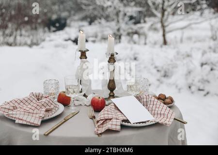 Cena romantica per due. Disposizione dei tavoli di Natale all'aperto. Bicchiere di vino, candele e tovaglioli a scacchi. Matrimonio invernale, San Valentino o compleanno Foto Stock