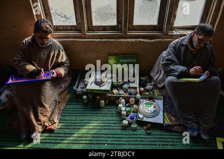 Srinagar, India. 7 dicembre 2023. Gli artigiani del Kashmir fanno i tocchi finali su un prodotto in cartapesta prima di inviarlo al mercato in un laboratorio. La cartapesta secolare, una forma d'arte profondamente intrecciata con la cultura e le tradizioni della società Kashmiri, sta morendo lentamente, poiché il numero di persone coinvolte nel commercio è diminuito per varie ragioni. Migliaia di famiglie in Kashmir si guadagnarono da vivere vendendo e facendo oggetti di cartapesta. L'emergere dell'arte della cartapesta accompagnò l'avvento dell'Islam nella regione. È stato introdotto in Kashmir dalla SUF Foto Stock