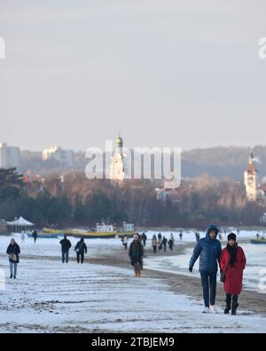 Gente che cammina lungo la spiaggia innevata di Danzica in una fredda giornata invernale sul Mar Baltico con Sopot resort città vista in lontananza, Polonia, Europa, UE Foto Stock