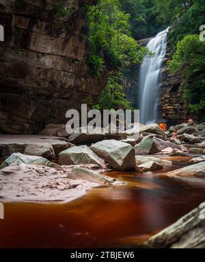 Paradiso nascosto: Cascata setosa in un canyon verdeggiante con i viaggiatori Foto Stock