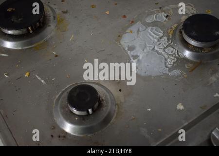 Foto non curata di stufa sporca in cucina con avanzi di cibo. Piano cottura a gas sporco con macchie di grasso, vecchie macchie di grasso, macchie di frittura e olio Foto Stock