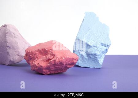 3 colorare pietre o ciottoli in tonalità di rosa, salmone e blu pastello isolate su uno sfondo bianco e viola. Fermi immagine minimi e fotografie vivaci Foto Stock