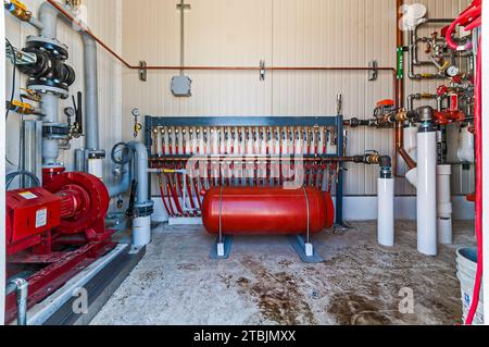 Un rack di valvole, tubi flessibili rossi e un serbatoio rosso in una piccola sala di controllo sul tetto di un magazzino di stoccaggio a freddo (refrigerazione industriale) a CO2. Foto Stock