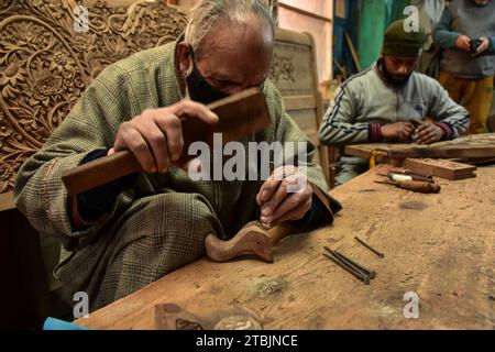 Srinagar, India. 7 dicembre 2023. Gli artigiani Kashmiri intagliano un oggetto artigianale in una fabbrica di intaglio del legno. Il Kashmir, il paradiso sulla terra, si riferisce alla bellezza naturale mozzafiato della regione e all'artigianato tradizionale. Insieme a molti altri tipi di arte, il Kashmir è rinomato per la sua tecnica unica di intaglio del legno. L'intaglio in legno Kashmiri è molto richiesto sia all'interno che all'esterno dello stato. Il suo mercato è cresciuto sia a livello locale che globale nel corso degli anni. Ma al giorno d'oggi, gli artigiani stanno lottando per mantenere viva questa arte. La maggior parte dei prodotti realizzati da questi artigiani non ottiene profitti sufficienti, a causa di W Foto Stock