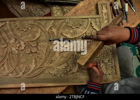 Srinagar, India. 7 dicembre 2023. Un artigiano Kashmiri intaglia un oggetto artigianale in una fabbrica di intaglio del legno. Il Kashmir, il paradiso sulla terra, si riferisce alla bellezza naturale mozzafiato della regione e all'artigianato tradizionale. Insieme a molti altri tipi di arte, il Kashmir è rinomato per la sua tecnica unica di intaglio del legno. L'intaglio in legno Kashmiri è molto richiesto sia all'interno che all'esterno dello stato. Il suo mercato è cresciuto sia a livello locale che globale nel corso degli anni. Ma al giorno d'oggi, gli artigiani stanno lottando per mantenere viva questa arte. La maggior parte dei prodotti realizzati da questi artigiani non ottiene abbastanza profitti, a causa di Foto Stock