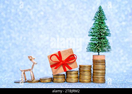 Allestimento creativo con gradini in pile di monete, adornati con un albero di Natale giocattolo, statuetta di cervo e una piccola confezione regalo, il tutto in un unico gioco Foto Stock