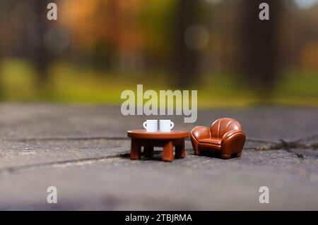 Vista ravvicinata di una poltrona in miniatura e di un tavolino da caffè con due tazze di caffè bianche su un ceppo di alberi in un ambiente boschivo. Piccolo rifugio nella foresta co Foto Stock