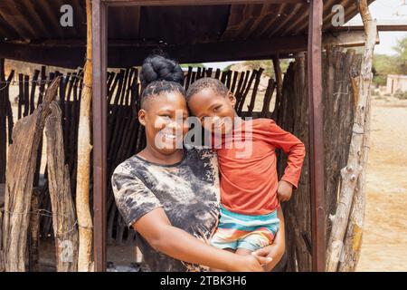 villaggio, famiglia africana in piedi di fronte alla baracca della cucina all'aperto nel cortile, madre e suo figlio Foto Stock