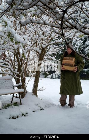 Uomo che porta legna da ardere attraverso la caduta di neve in giardino per uso come combustibile in un bruciatore di legno Zala county Ungheria Foto Stock