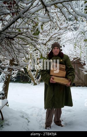 Uomo che porta legna da ardere attraverso la caduta di neve in giardino per uso come combustibile in un bruciatore di legno Zala county Ungheria Foto Stock