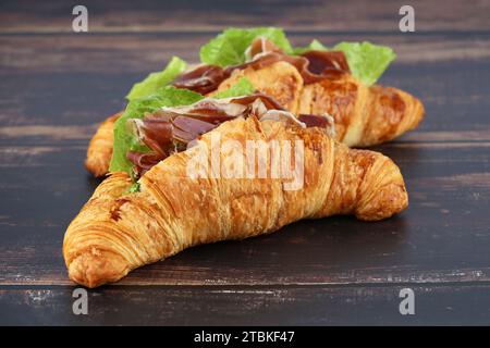 Panini con croissant con prosciutto e lattuga su tavola di legno. Foto Stock