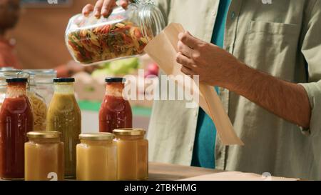 Cliente riempie il sacchetto di carta con pasta per acquistare la giusta quantità per un pasto sano, versando prodotti biologici naturali venduti come prodotti sfusi in vasetti riutilizzabili. Un uomo che va a fare la spesa. Scatto manuale. Foto Stock