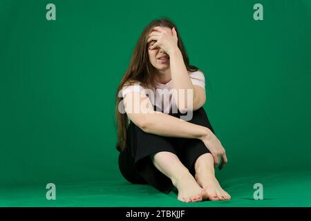 Una giovane donna che scuote la testa in furia e piange su uno sfondo verde. Colpo medio. Foto di alta qualità Foto Stock