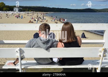 Spiaggia di Sopot Polonia giovane coppia seduta su una panchina sul molo di Sopot affacciata sulla spiaggia fuori stagione a Sopot, Pomerania, Polonia, Europa, UE Foto Stock