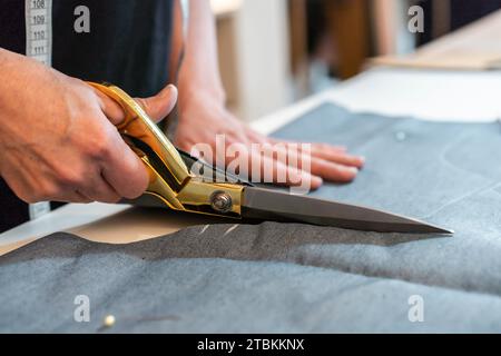 Primo piano delle mani dei designer di moda utilizzando le forbici per tagliare i tessuti sul tavolo da lavoro. Foto Stock