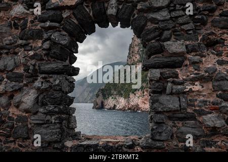 Finestra in pietra ad arco o apertura su un muro di pietra che si affaccia sul paesaggio panoramico del mare e delle montagne liguri a Portovenere, Italia. Foto Stock