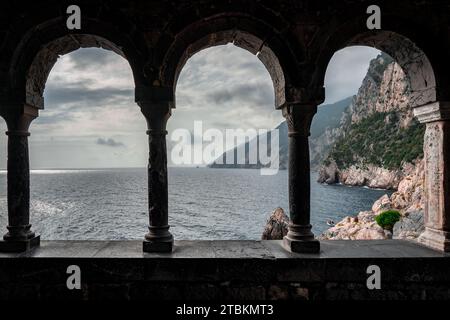 Finestra in pietra ad arco o apertura su un muro di pietra che si affaccia sul paesaggio panoramico del mare e delle montagne liguri a Portovenere, Italia. Foto Stock