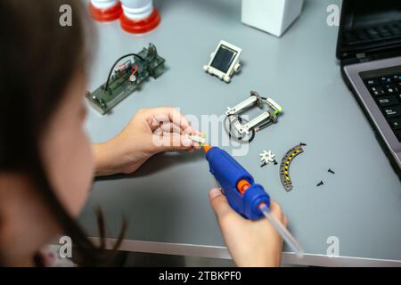 Studente che utilizza una pistola per colla a caldo su pezzi di macchine in classe di robotica Foto Stock