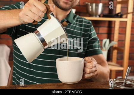 Uomo che versa il caffè aromatico della moka in una tazza al tavolo all'interno, primo piano Foto Stock