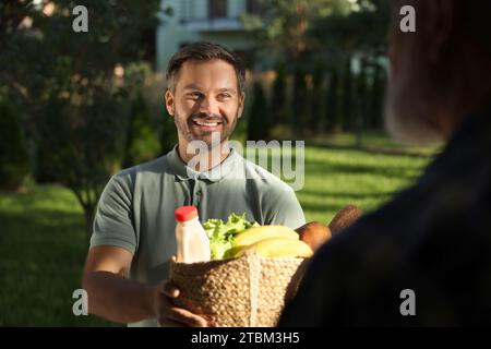 Uomo con un sacco di prodotti in vimini che aiuta il suo vicino più anziano all'aperto Foto Stock