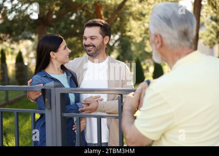 Rapporto amichevole con i vicini. Coppia felice e uomo anziano vicino alla recinzione all'aperto Foto Stock