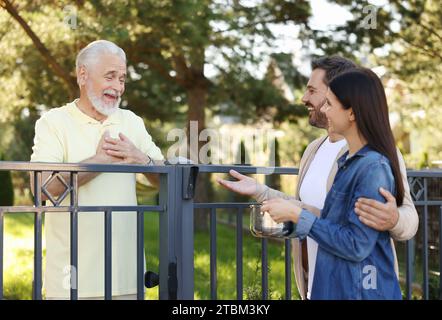 Rapporto amichevole con i vicini. Coppia felice e uomo anziano vicino alla recinzione all'aperto Foto Stock