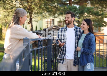 Rapporto amichevole con i vicini. Felice giovane coppia che parla con una donna anziana vicino alla recinzione all'aperto Foto Stock