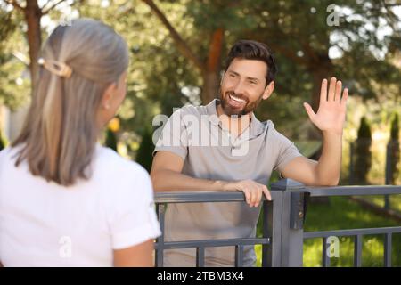 Rapporto amichevole con i vicini. Uomo felice che saluta donna anziana vicino a recinzione all'aperto Foto Stock