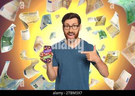 La tua scommessa vince! Uomo emotivo che punta lo smartphone sotto la doccia di denaro su sfondo colorato Foto Stock