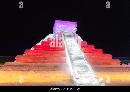 HARBIN, CINA - 1° gennaio 2022: Costruzione di ghiaccio a forma di piramide messicana. Harbin International Ice and Snow Festival. I turisti sono in visita. Loca Foto Stock