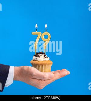 Dolce di compleanno consegnato a mano - candela numero 79 su sfondo blu Foto Stock