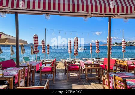 Ombrelloni da spiaggia, lettini, tavoli e sedie sulla riva di una tranquilla baia blu al mattino presto. Vacanze estive e destinazione per le vacanze Foto Stock