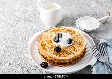 Una grande pila di deliziosi pancake caldi con panna acida e more su un bellissimo vassoio bianco Una delizia tradizionale per il Festival. Foto Stock