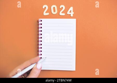 La mano di un bambino con la penna su un quaderno bianco e la scrittura della lista dei desideri. Obiettivi di pianificazione della persona, attività per il nuovo anno 2024 scrivendo la lista delle attività su Foto Stock