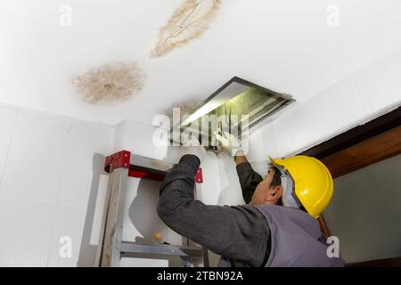 Il lavoratore ripara il tubo che perde nel soffitto, primo piano di una macchia sul soffitto. Foto Stock