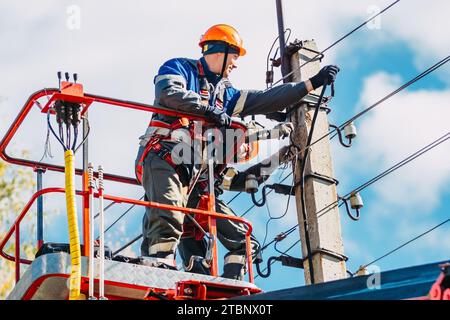 Due elettricisti professionisti con elmetti stanno riparando le linee elettriche dalla base del dumper a benna. Foto Stock