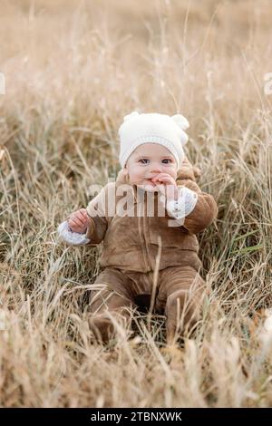 Bambino sorridente di 9 mesi in costume da orso che mangia erba in campo autunnale Foto Stock