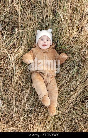 Bambino felice di 9 mesi che indossa un abito da orso adagiato in erba autunnale Foto Stock