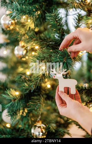 Mani che posizionano ornamenti in legno di rodolfo su un albero illuminato Foto Stock