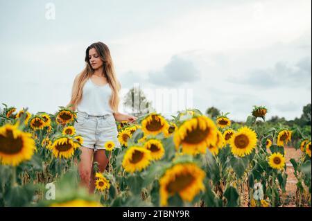 Giovane donna caucasica con capelli biondi che cammina attraverso un campo fiorito. Foto Stock