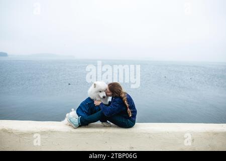 La ragazza cammina con un cane Samoyed bianco e soffice in natura Foto Stock