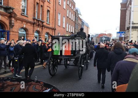 La processione funebre di Shane MacGowan che passa davanti a Lincoln Place mentre attraversa le strade di Dublino prima del suo funerale nella Co Tipperary. Il cantautore, che ha trovato fama come cantante principale della band punk/folk londinese The Pogues, è morto all'età di 65 anni la settimana scorsa. Data immagine: Venerdì 8 dicembre 2023. Foto Stock