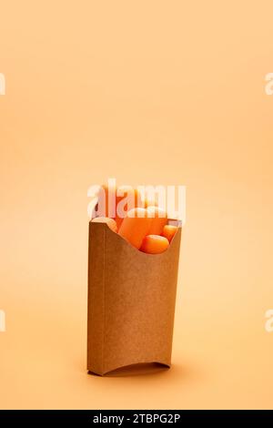 Carote tagliate, fresche e deliziose, inserite nella confezione di cartone per le patatine fritte su sfondo arancione. Prodotti biologici e cibo sano Foto Stock