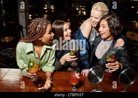 ragazze multietniche eccitate e alla moda con cocktail che parlano al bar, atmosfera vivace Foto Stock