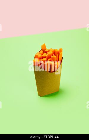 Carote fresche tagliate inserite nella confezione di cartone per le patatine fritte su sfondo verde. Prodotti biologici e cibo sano Foto Stock