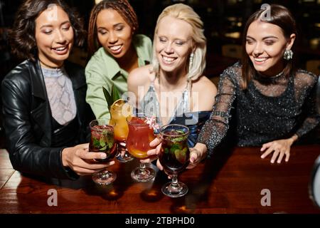 eccitanti amiche multiculturali che bevono bicchieri da cocktail durante il tempo libero al bar, piacere Foto Stock