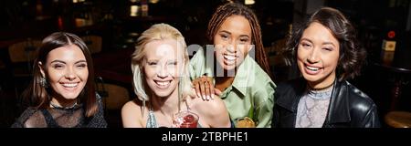 amiche multietniche eleganti e felici con bicchieri da cocktail sorridenti al bar, banner Foto Stock